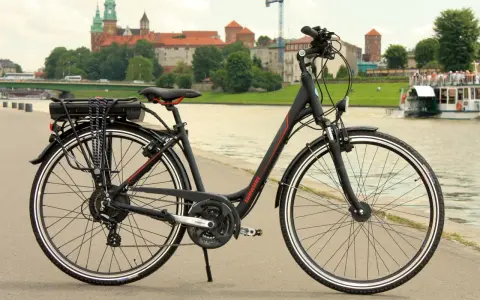 Czarny rower elektryczny z baterią na bagażniku, gotowy do jazdy po bulwarach z widokiem na Wawel.