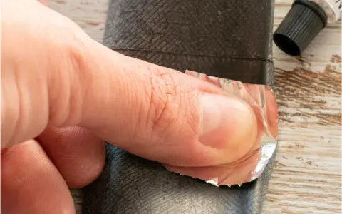 Dłoń przykleja łatkę do dętki roweru z przerzutką w piaście.
