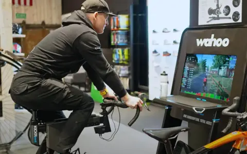 Mężczyzna na rowerze stacjonarnym z napędem **direct drive** wirtualnie przemierza trasę, widoczną na ekranie Wahoo.
