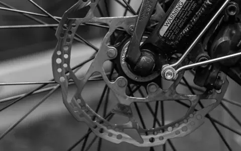 Zbliżenie na tarczę hamulcową i piastę roweru. Widać mechanizm przerzutki Shimano i ostrzeżenie na ramie.