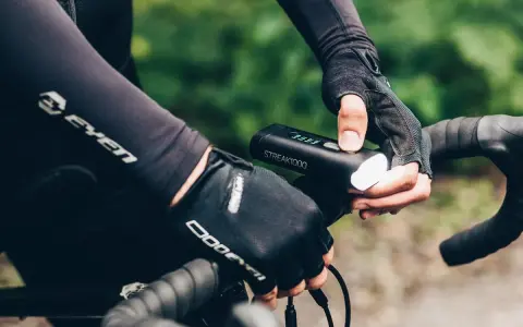 Rowerzysta w rękawiczkach sprawdza mocne oświetlenie rowerowe STREAK1000. Dobre oświetlenie to podstawa bezpieczeństwa.