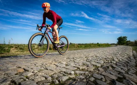 Kobieta w kasku i okularach jedzie na rowerze BMC URS LT po brukowanej drodze.