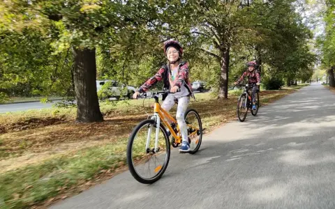 Dzieci na rowerach 24 cale na jaki wzrost? Uśmiechnięta dziewczynka na pomarańczowym rowerze i jej koleżanka cieszą się jazdą po alei.