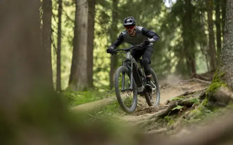 Rowerzysta w kasku i okularach zjeżdża po wyboistej leśnej ścieżce. To właśnie jest **co to enduro** – jazda po trudnym terenie.