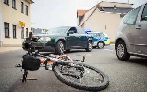 Wypadek drogowy: przewrócony rower, samochód i radiowóz policyjny. Maksymalne obciążenie roweru mogło przyczynić się do zdarzenia.