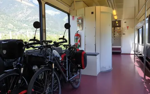 Dwa rowery z sakwami czekają na podróż. Widać okno z widokiem na góry. To praktyczny sposób, jak powiesić rower w pociągu.