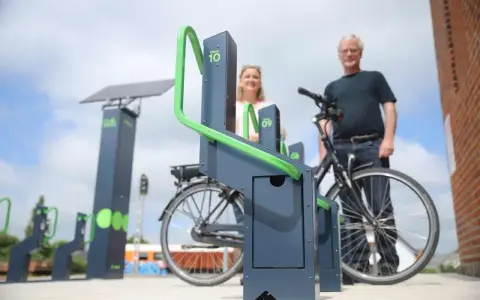 Stacja ładowania rowerów elektrycznych zasilana energią słoneczną. Para ludzi korzysta z nowoczesnych stojaków.