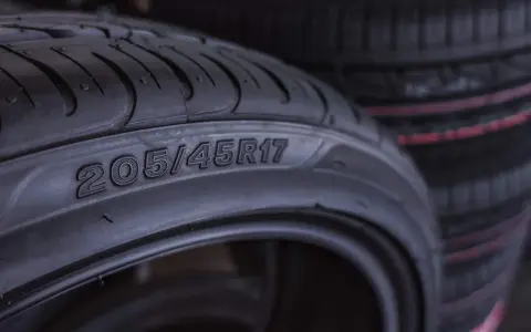 Zbliżenie na oponę z widocznymi oznaczeniami 205/45R17. W tle widać stos innych opon.