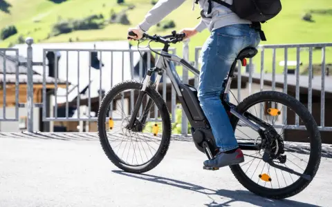 Osoba na rowerze elektrycznym, korzystająca z dofinansowania PFRON. W tle zielone wzgórza i zabudowania.