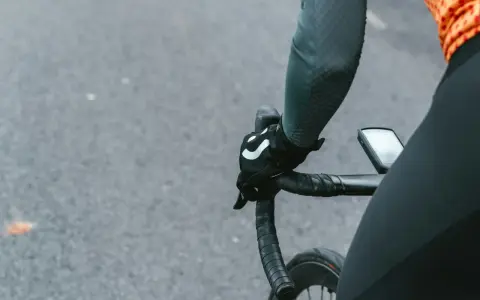Rowerzysta w rękawiczkach z logo, trzymający kierownicę szosową. Kluczowe jest, jak dobrać szerokość kierownicy szosowej dla komfortu.