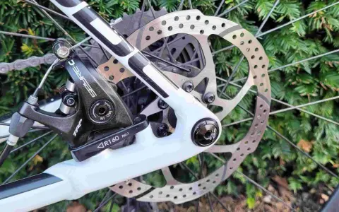 Regulacja hamulca tarczowego mechanicznego w rowerze. Widoczny zacisk TRP, tarcza hamulcowa i fragment ramy.