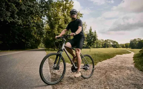 Mężczyzna w kasku i okularach jedzie na rowerze typu cross po leśnej ścieżce.