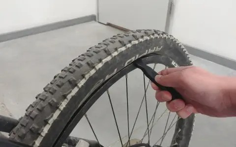 Dłoń używa łyżki do opon do wymiany opony w rowerze.