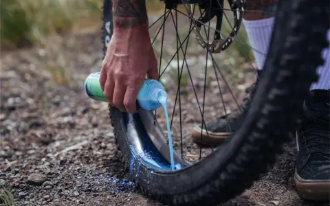 Ręka wylewa mleczko do opony rowerowej. To część przygotowania systemu **radial tubeless**, który zapewnia lepszą przyczepność i odporność na przebicia.