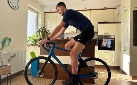 Mężczyzna w stroju kolarskim ćwiczy na rowerze gravel w domu. Poprawna pozycja na rowerze gravel jest kluczowa dla komfortu i wydajności.