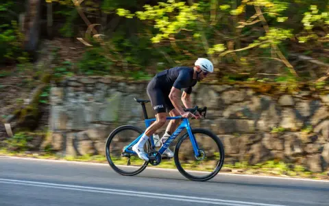 Kolarz w kasku ściga się na niebieskim rowerze Canyon Endurace CF 7 po malowniczej drodze wśród zieleni.