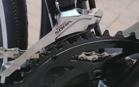 Montaż przedniej przerzutki Shimano Sora na rowerze. Widoczny fragment mechanizmu korbowego i łańcucha.