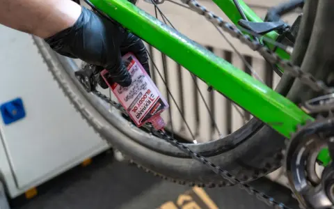 Rękawiczka z czarną gumką aplikuje różowy olej do łańcucha roweru. To część przeglądu roweru, aby zapewnić płynną jazdę.