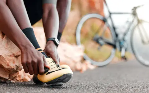 Rowerzysta zapina żółte buty, gotowy na kolejne wyzwania w **sporty rowerowe**. W tle widać rower.
