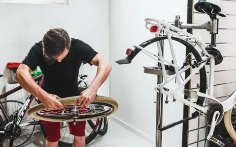 Mężczyzna w czarnym t-shircie i czerwonych spodenkach naprawia rower, przygotowując się do montażu chwytów na kierownicę.