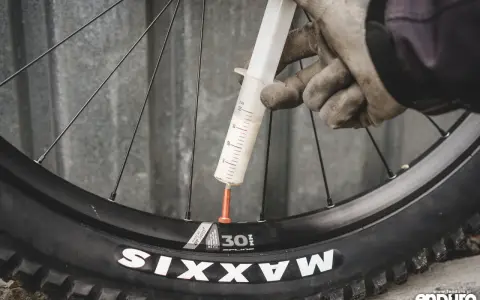 Rękawiczki i strzykawka z mleczkiem uszczelniającym przy wentylu koła rowerowego. Przygotowanie do **prostowania felg rowerowych** i uszczelnienia opony.