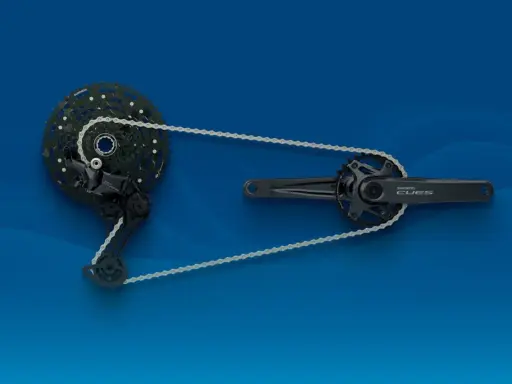 Zestaw napędowy **Shimano CUES**: przerzutka tylna, kaseta i korba z zębatkami, połączone łańcuchem na niebieskim tle.