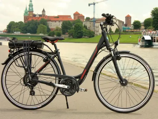 Czarny rower elektryczny z baterią na bagażniku, gotowy do jazdy po bulwarach z widokiem na Wawel.