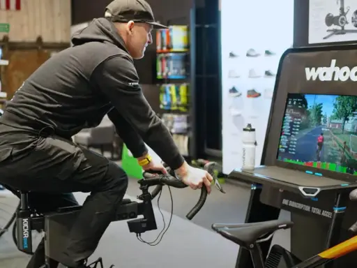 Mężczyzna na rowerze stacjonarnym z napędem **direct drive** wirtualnie przemierza trasę, widoczną na ekranie Wahoo.