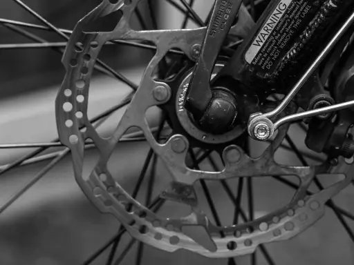 Zbliżenie na tarczę hamulcową i piastę roweru. Widać mechanizm przerzutki Shimano i ostrzeżenie na ramie.