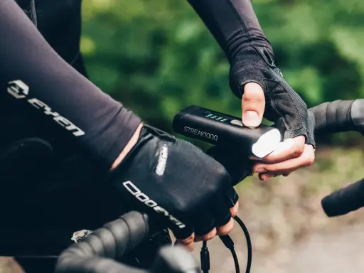 Rowerzysta w rękawiczkach sprawdza mocne oświetlenie rowerowe STREAK1000. Dobre oświetlenie to podstawa bezpieczeństwa.