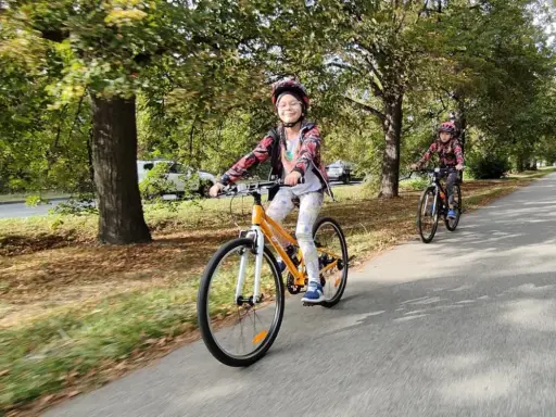Dzieci na rowerach 24 cale na jaki wzrost? Uśmiechnięta dziewczynka na pomarańczowym rowerze i jej koleżanka cieszą się jazdą po alei.