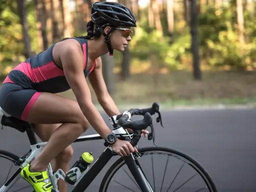 Kobieta w kasku i okularach przeciwsłonecznych pedałuje na rowerze szosowym przez las. Widać jej nogi w sportowym stroju i zegarek na ręce. To efekty po miesiącu regularnej jazdy na rowerze.