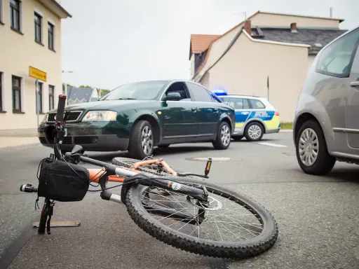 Wypadek drogowy: przewrócony rower, samochód i radiowóz policyjny. Maksymalne obciążenie roweru mogło przyczynić się do zdarzenia.