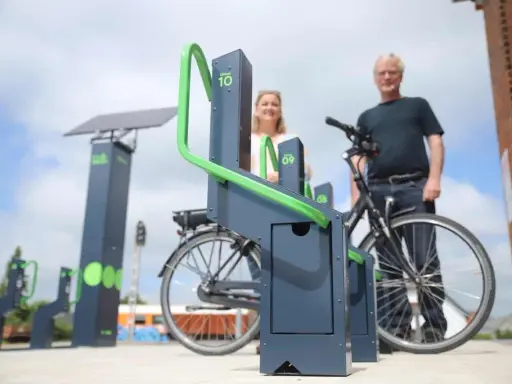 Stacja ładowania rowerów elektrycznych zasilana energią słoneczną. Para ludzi korzysta z nowoczesnych stojaków.