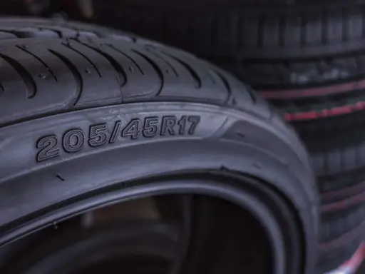 Zbliżenie na oponę z widocznymi oznaczeniami 205/45R17. W tle widać stos innych opon.