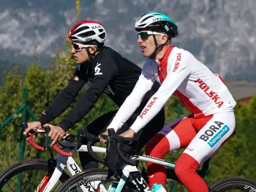 Dwóch kolarzy, być może najlepsi kolarze w historii, w biało-czerwonych strojach z napisem "Polska" i logiem "Bora Hansgrohe", ściga się na tle gór.