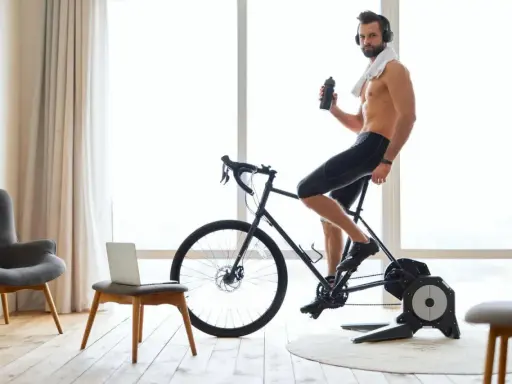 Mężczyzna w słuchawkach pije wodę, ćwicząc na rowerze stacjonarnym przy dobrej muzyce na rower.