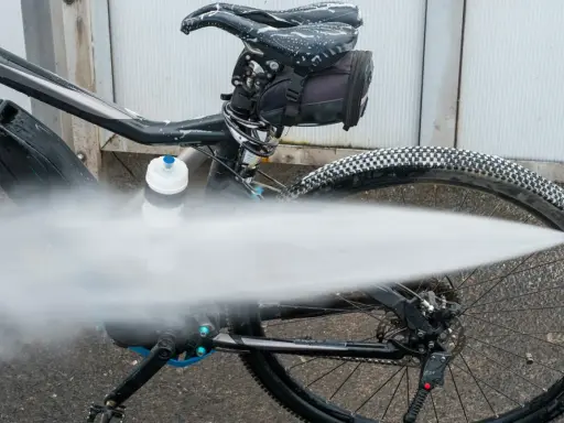 Czyszczenie roweru na myjni. Silny strumień wody spłukuje brud z opon i ramy.
