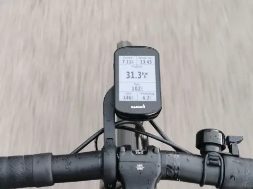 Na kierownicy roweru zamontowany jest licznik Garmin, który pokazuje dystans 7.11 km, tętno 146, rytm 102, temperaturę 6.2°C i aktualny czas 13:43. Prędkość 31.3 km/h jest widoczna na ekranie.
