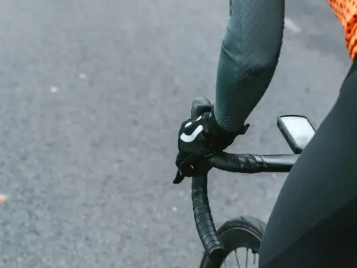 Rowerzysta w rękawiczkach z logo, trzymający kierownicę szosową. Kluczowe jest, jak dobrać szerokość kierownicy szosowej dla komfortu.