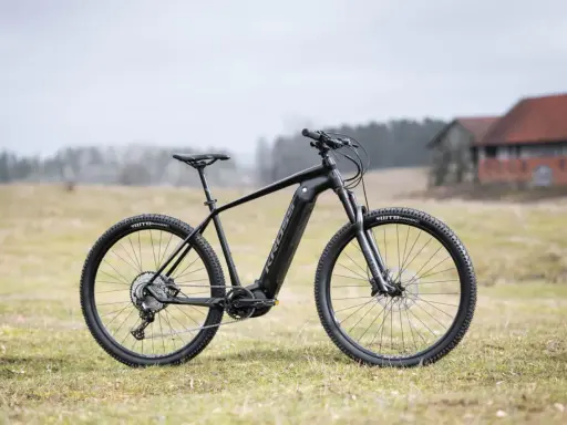Czarny rower Kross Level Boost 3.0 z napędem elektrycznym stoi na trawie. W tle budynki i drzewa.