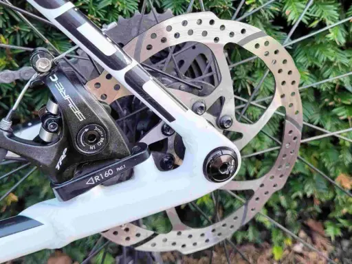 Regulacja hamulca tarczowego mechanicznego w rowerze. Widoczny zacisk TRP, tarcza hamulcowa i fragment ramy.