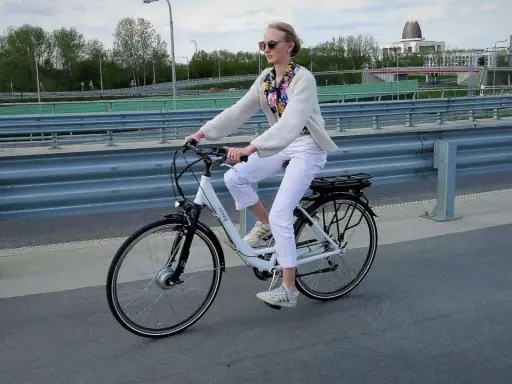 Kobieta na rowerze elektrycznym, ubrana na biało, jedzie po moście. Uważaj na przepisy, by nie dostać mandatu za rower elektryczny.