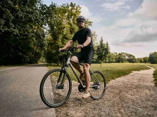Mężczyzna w kasku i okularach jedzie na rowerze typu cross po leśnej ścieżce.