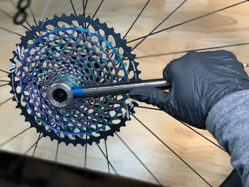 Rękawiczka w czarnej rękawiczce dokręca nową, tęczową kasetę SRAM Eagle. Wymiana wolnobiegu na kasetę zakończona sukcesem!