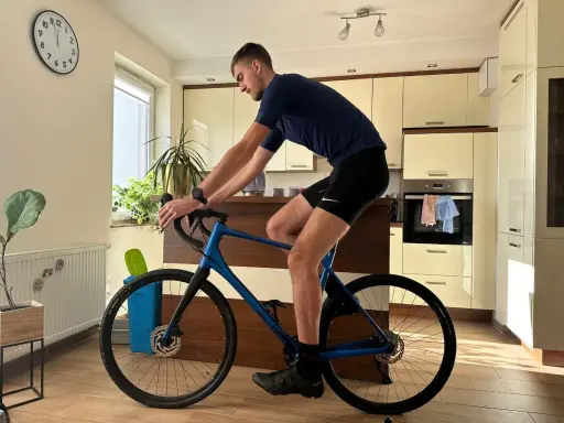 Mężczyzna w stroju kolarskim ćwiczy na rowerze gravel w domu. Poprawna pozycja na rowerze gravel jest kluczowa dla komfortu i wydajności.