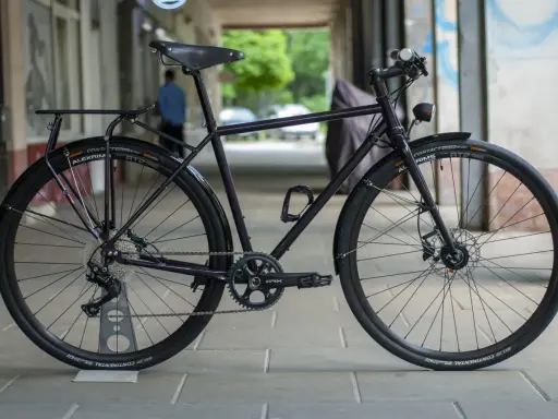 Ciemny rower gravel z błotnikami, bagażnikiem i oświetleniem, gotowy na każdą trasę.