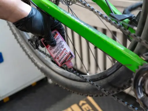 Rękawiczka z czarną gumką aplikuje różowy olej do łańcucha roweru. To część przeglądu roweru, aby zapewnić płynną jazdę.