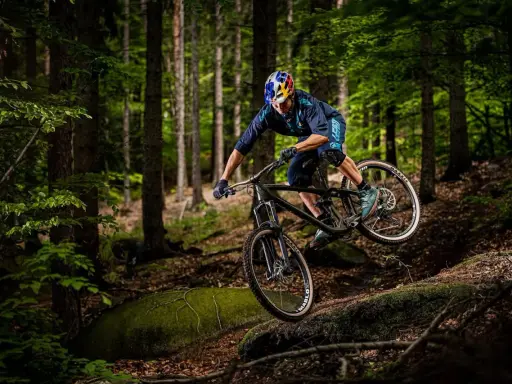 Kolarz w kasku Red Bull zjeżdża rowerem po leśnym stoku. To jest właśnie downhill – szybka jazda w dół!