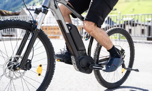 Mężczyzna pedałuje na rowerze elektrycznym, pokazując, jak działa rower elektryczny. Bateria i silnik są widoczne na ramie.